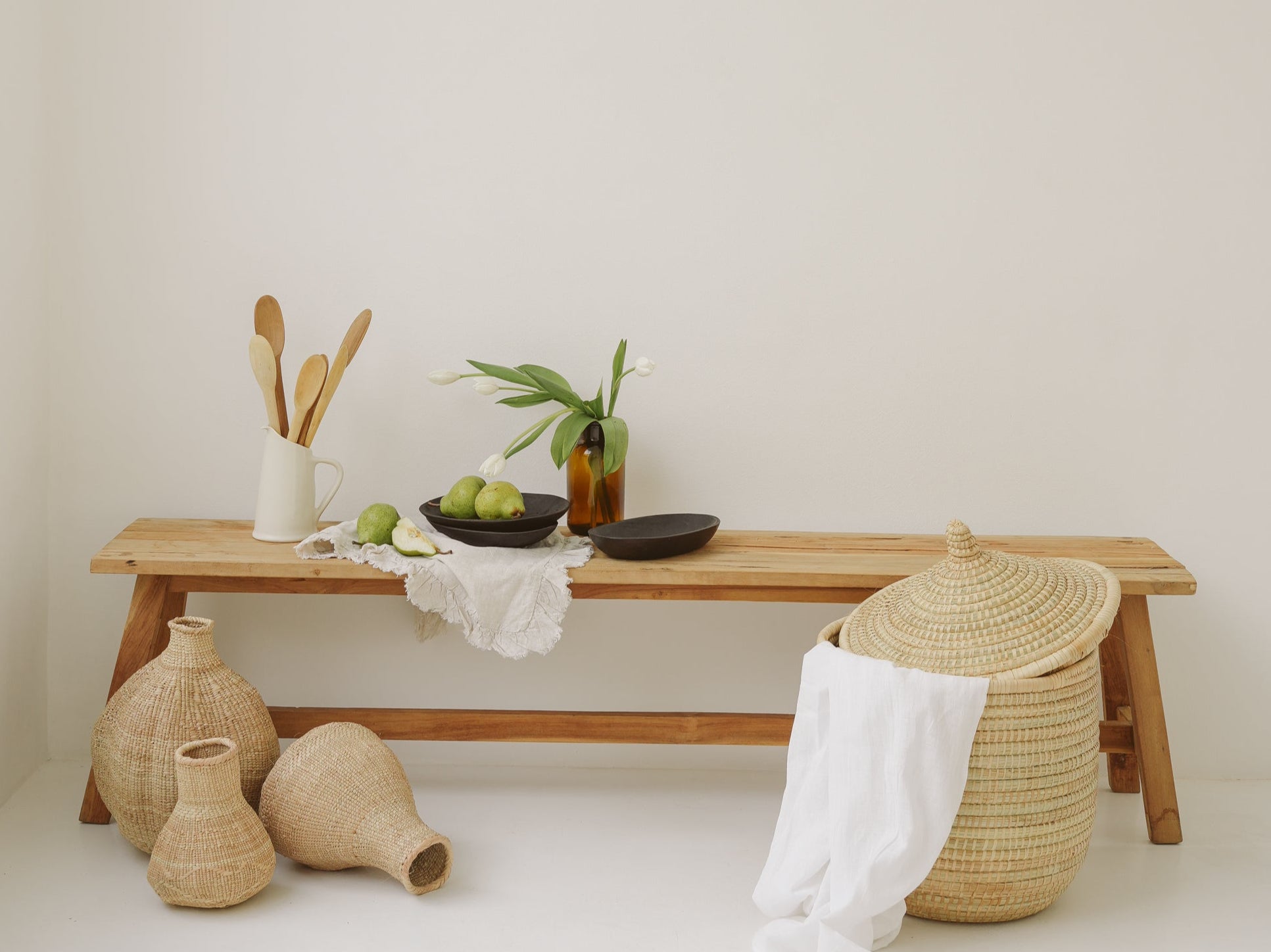 Minimalist interior with wooden bench, vases, and a basket against a white wall.
