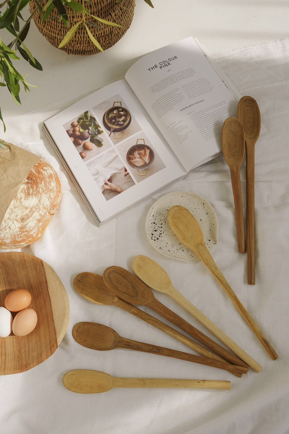 Wooden spoons on a white surface with a cookbook and eggs in the background